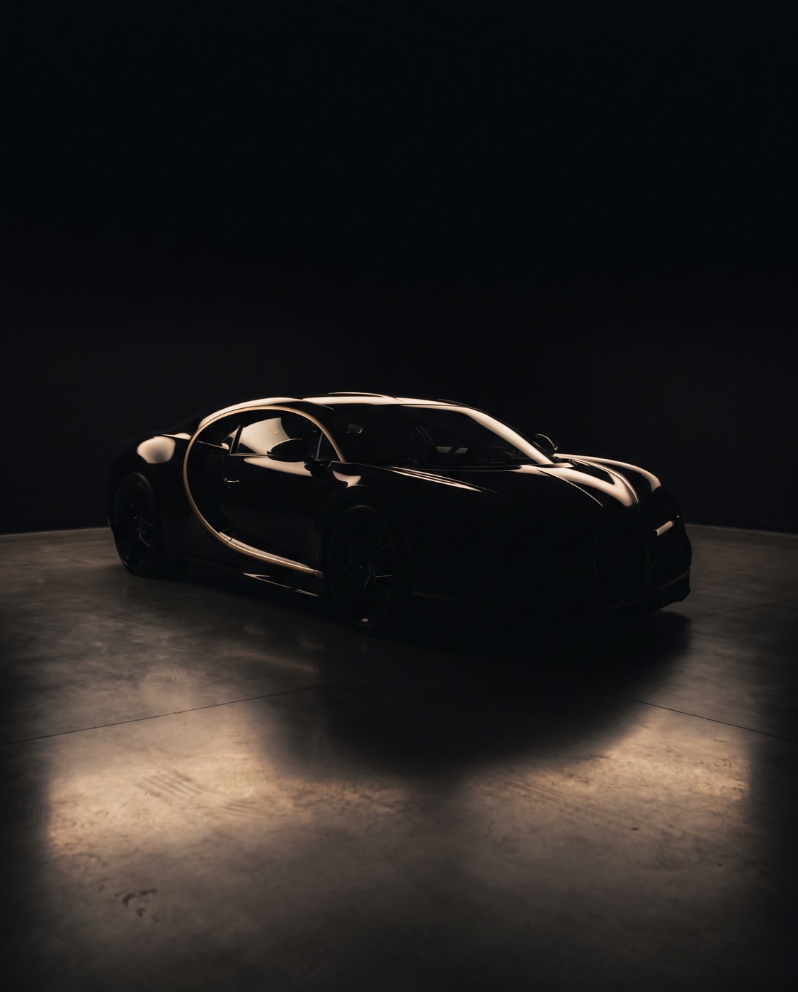 Schwarzer Supersportwagen in dunklem Showroom, von warmem Lichtstreifen konturiert